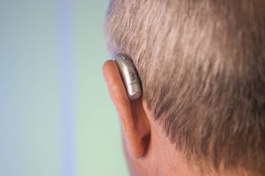 Kafkasyalı beyaz yaşlı adam kulağına modern dijital işitme cihazı takıyor ve gri saçlı..