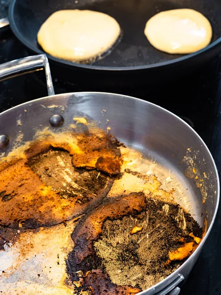 steel stewpan with crust of food burned while frying pancakes on electric stove in home kitchen