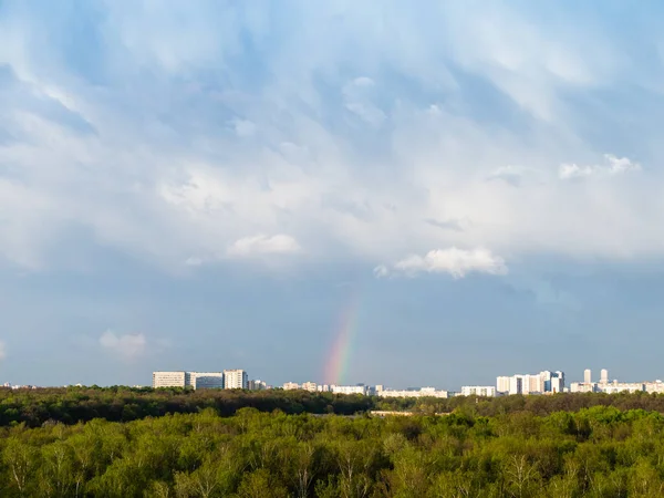 blue rainy clouds and rainbow over city on sunny spring day