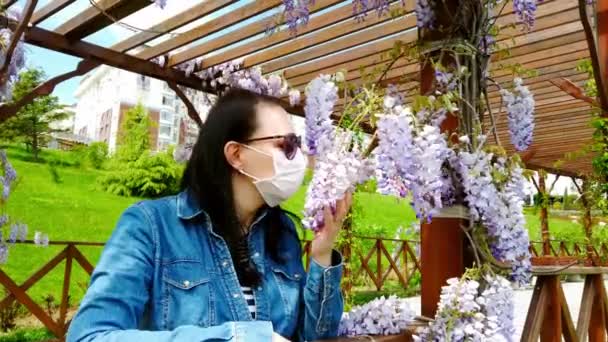 Brunette-jente i medisinsk maske med bakgrunn fra blomstrende magnolia . – stockvideo