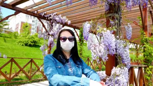 Brunette-jente i medisinsk maske med bakgrunn fra blomstrende magnolia . – stockvideo