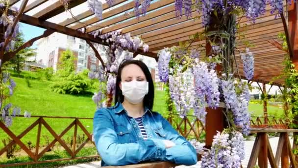 Bruna ragazza in maschera medica su sfondo di magnolia in fiore . — Video Stock