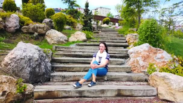 Mladá žena sedí na širokých kamenných schodech v městském parku. — Stock video