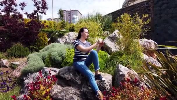 Fiatal nő ül nagy kő sziklák a városi parkban. — Stock videók