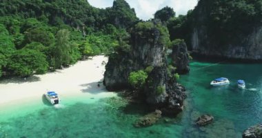 Adanın sahilinde bir dron. Kumlu sahil ve bitkilerle dolu kayalar. Tekneler.