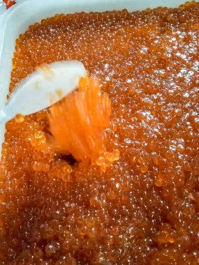 Plastik kabın içinde kırmızı havyar. Plastik kaşıkla karıştırıyor.