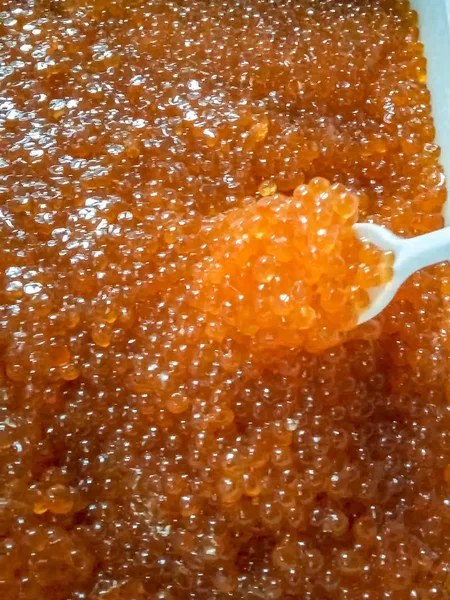 Caviar rojo en un recipiente de plástico. Agitación con una cuchara de plástico o —  Fotos de Stock