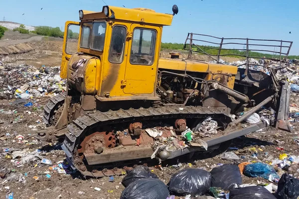 Un bulldozer cancella mucchi di spazzatura in un bidone della spazzatura. Bulldozer di lavoro in una discarica . — Foto Stock