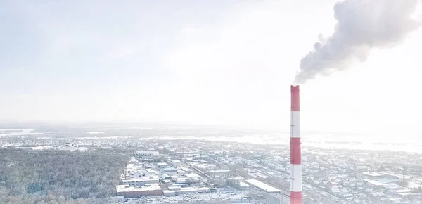 Kouřící komín tepelné elektrárny na pozadí zimního města. — Stock fotografie