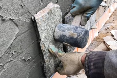 İnşaatçı elinde vahşi bir taş olan bir evin bodrumuna bakıyor. Düz fo