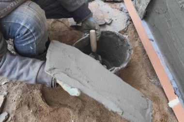 İnşaatçı elinde vahşi bir taş olan bir evin bodrumuna bakıyor. Düz fo