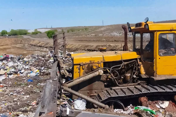 A bulldozer clears heaps of garbage in a garbage can. Work bulld