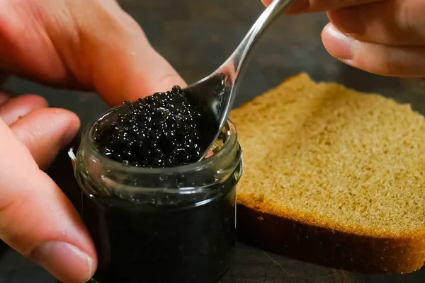 Omrøring sort kaviar med en ske i glas krukke . - Stock-foto