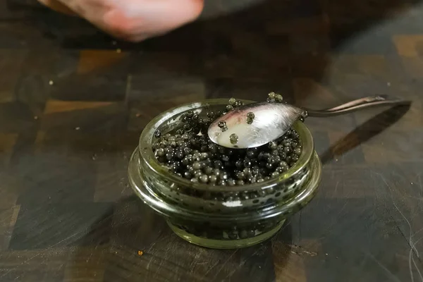 Schwarzer Kaviar mit einem Löffel im Glas rühren. — Stockfoto