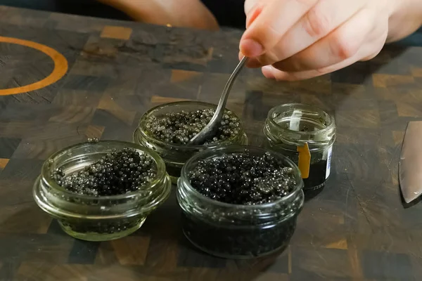 Stirring black caviar with a spoon in glass jar. — Stock Photo, Image