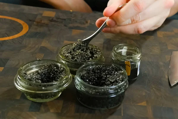 Stirring black caviar with a spoon in glass jar. — Stock Photo, Image