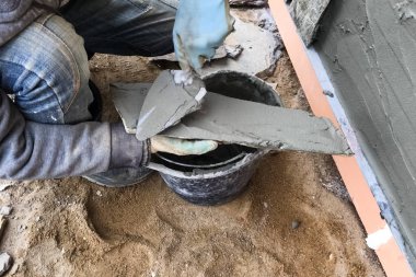 İnşaatçı elinde vahşi bir taş olan bir evin bodrumuna bakıyor. Düz fo