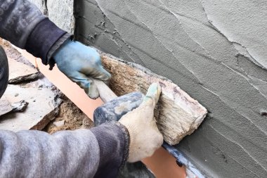 İnşaatçı elinde vahşi bir taş olan bir evin bodrumuna bakıyor. Düz fo