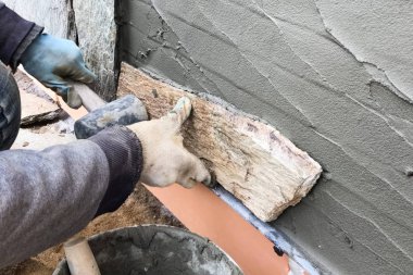 İnşaatçı elinde vahşi bir taş olan bir evin bodrumuna bakıyor. Düz fo