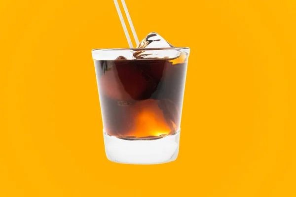 Vidro com cola com gelo e palha sobre um fundo laranja . — Fotografia de Stock