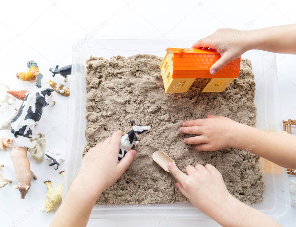 Montessori material. Children's hands play an animal figure. Kinetic sand