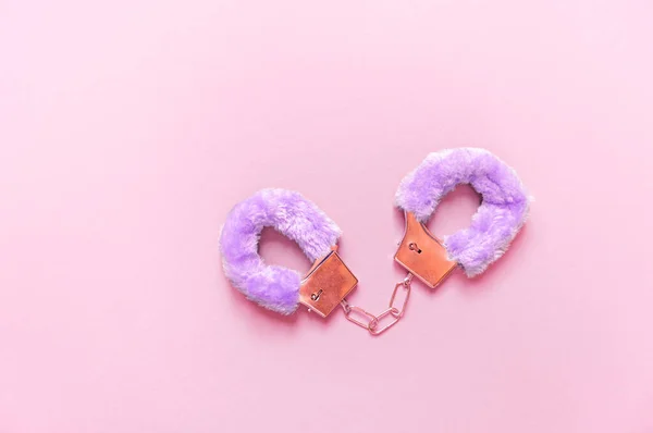 Handboeien met paars haar volwassen seksspeeltjes, minimaal design, geïsoleerd op een roze achtergrond. — Stockfoto
