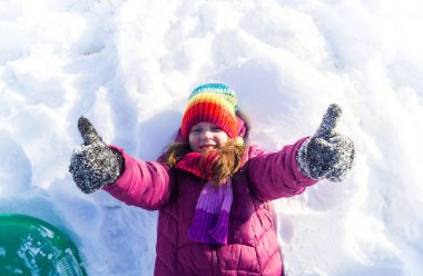 Çocuk karda sırt üstü yatıyor. Duygu sömürücü kız ellerini kaldırır. Kış tatili Açık hava oyunları.