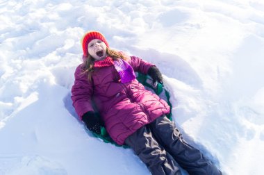 Bir çocuk karlı bir tepeden yuvarlanıyor. Yürüyüş yapan duygusal kız. Kış tatili Açık hava oyunları.