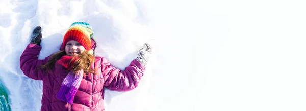 El niño yace boca arriba en la nieve. Emoción chica en un paseo. Vacaciones de invierno. Juegos al aire libre. Copiar espacio Banner — Foto de Stock