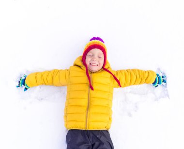 Sarı ceketli çocuk beyaz karda yatıyor.