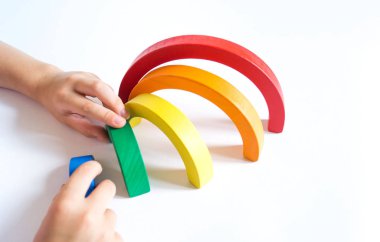 Montessori ahşap gökkuşağı malzemesi. Bir çocuk elleriyle bir oyuncakla oynar..