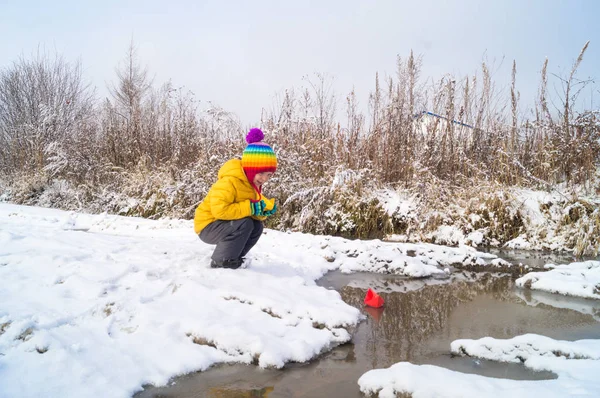 Un niño lanza un barco de papel en un arroyo en invierno — Foto de Stock