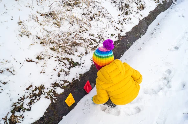 Un niño lanza un barco de papel en un arroyo en invierno — Foto de Stock