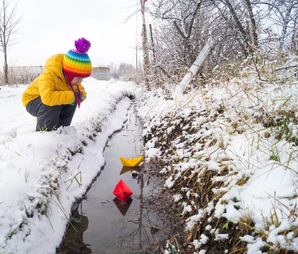 Un niño lanza un barco de papel en un arroyo en invierno — Foto de Stock