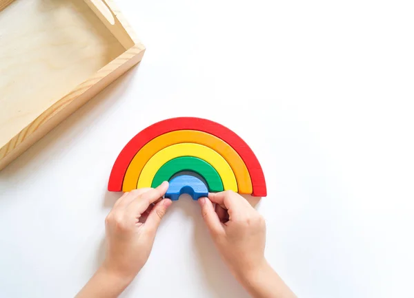 Montessori material arco-íris de madeira. Uma criança brinca com um brinquedo com as mãos . — Fotografia de Stock