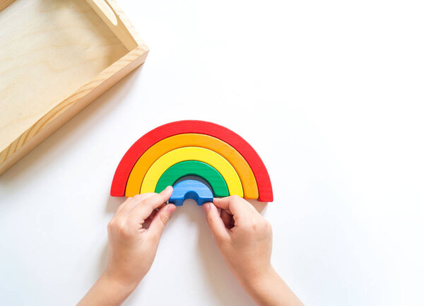 Montessori wood rainbow material. A child plays with a toy with his hands.
