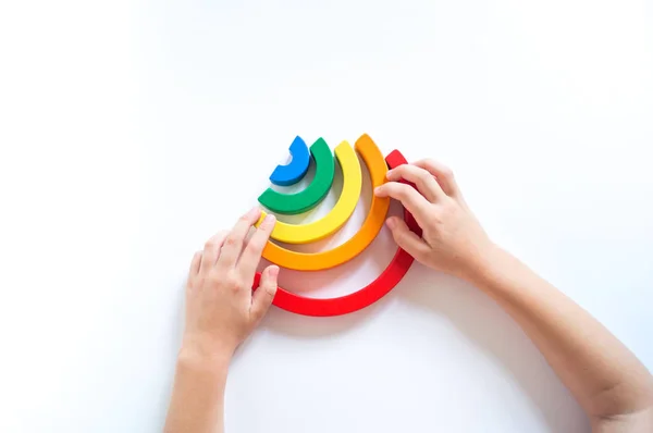 Material de madera Montessori arco iris. Un niño juega con un juguete con las manos . — Foto de Stock