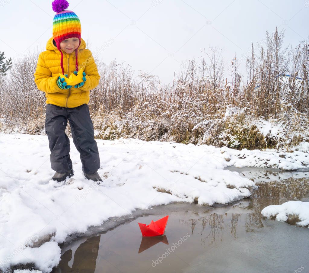 A child launches a paper boat on a stream in winter