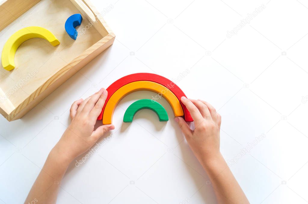 Montessori wood rainbow material. A child plays with a toy with his hands.