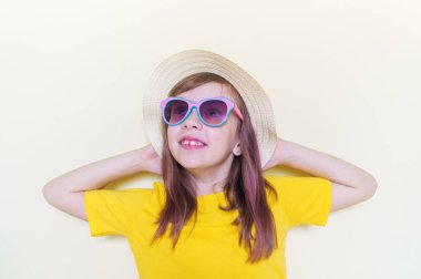 The child sits in the room on the floor emotion on his face. Little girl in a yellow T-shirt, glasses and a straw hat.