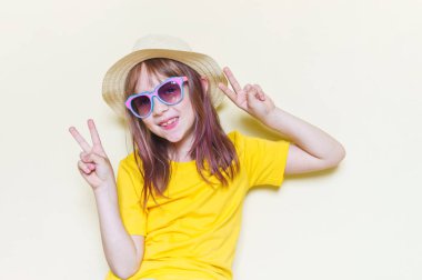 The child sits in the room on the floor emotion on his face. Little girl in a yellow T-shirt, glasses and a straw hat.