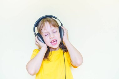 The child sits in the room and listens to music and sings . Little girl in a yellow T-shirt.