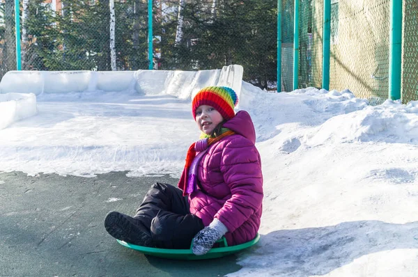 El niño rueda por un tobogán de hielo. Ropa brillante sombrero de arco iris . — Foto de Stock
