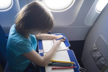 child draws with pencils while sitting in an airplane.