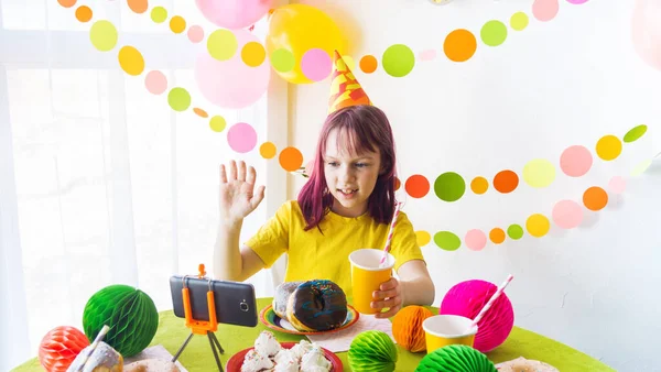 Children virtual birthday party with cake online together with her friend in video conference. With digital telephone for a online meeting. Girl celebrating birthday online in quarantine time