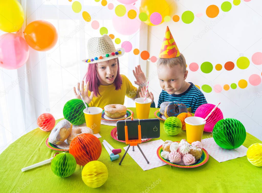Children virtual birthday party with cake online together with her friend in video conference. With digital telephone for a online meeting. Girl and boy celebrating birthday online in quarantine time
