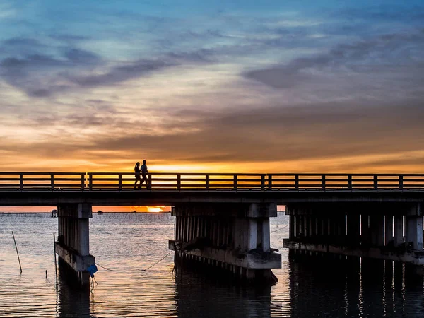 Silhueta de pessoas não identificadas caminham na ponte, pôr do sol tim — Fotografia de Stock