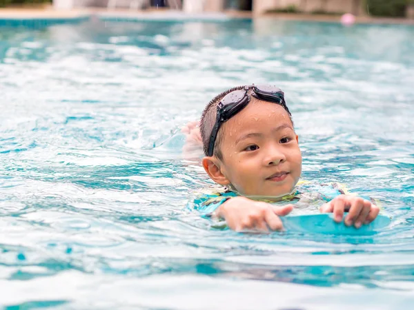 亚洲男孩游泳与板在水池里 — 图库照片