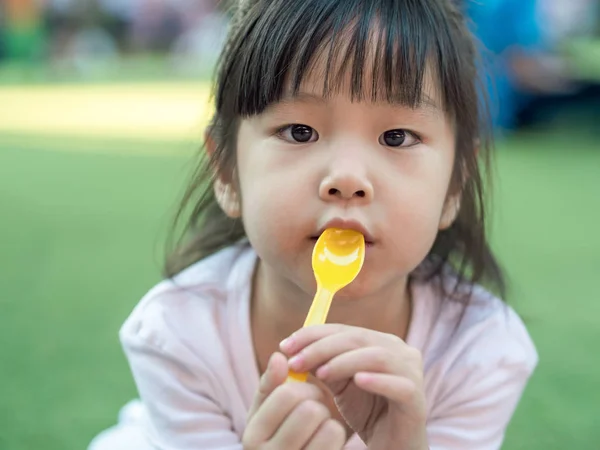 Азиатская девочка ест десерт, ложка во рту — стоковое фото