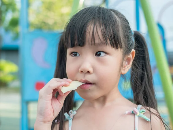 Азиатский ребенок играет на детской площадке, едят манго — стоковое фото